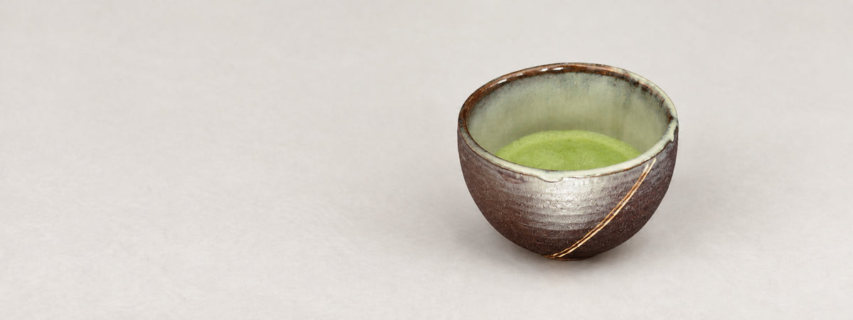 Ceramic bowl with gold details and natural green matcha on a light background.
