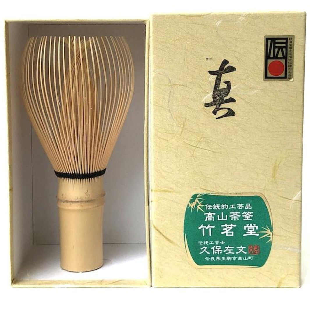 A bamboo matcha whisk shown inside an open presentation box next to its beige outer packaging, with Chinese and Japanese branding on the box.